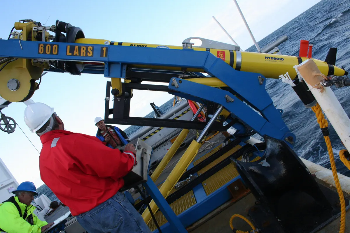 Two U.S. Navy oceanographic surveyors prepare to launch a yellow Remus 600 autonomous underwater vehicle from a ship deck